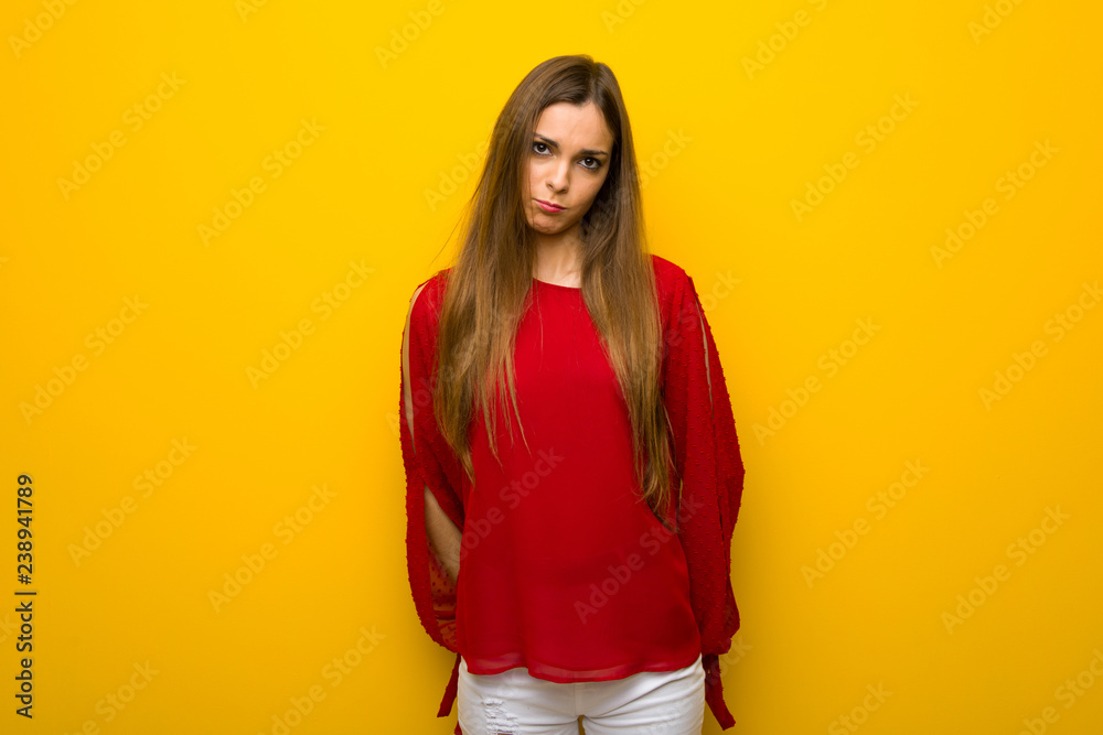 Young girl with red dress over yellow wall with sad and depressed expression Young girl with red dress over yellow wall with sad and depressed expression
