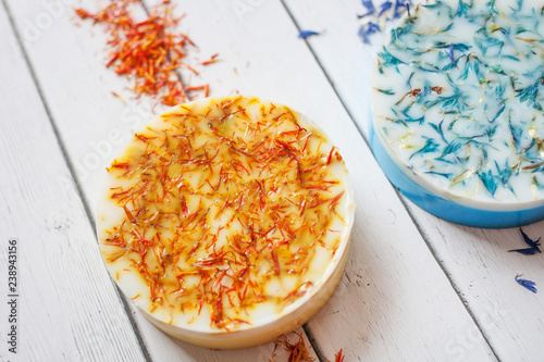 cropped photo of a round piece of handmade soap with orange dried flowers of calendula on a white wooden background photo