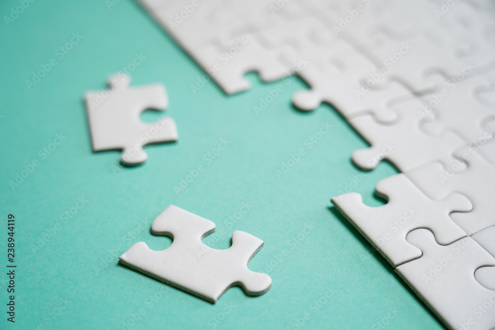 Fragment of a folded white jigsaw puzzle and a pile of uncombed puzzle elements against the background of a colored surface. Fragment of a folded white jigsaw puzzle and a pile of uncombed puzzle elements against the background of a colored surface.