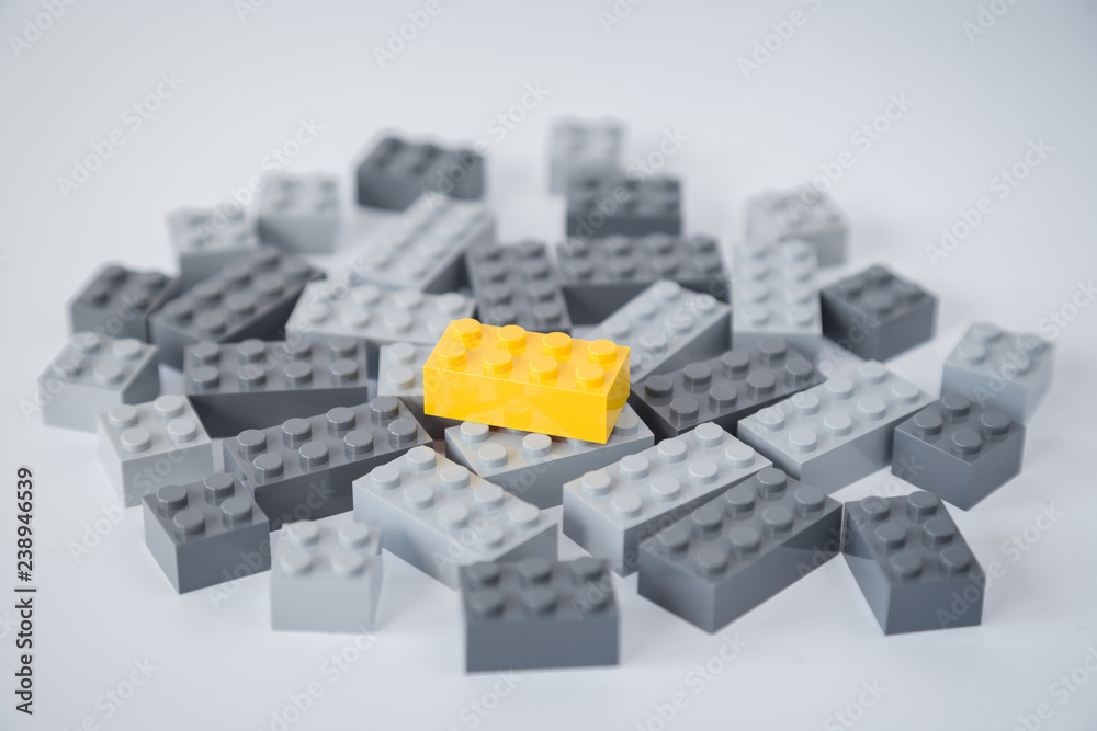 Pile of gray toy building bricks and one bright yellow brick on top of them on light gray background. Concept photo of standing out from the crowd or gray masses.