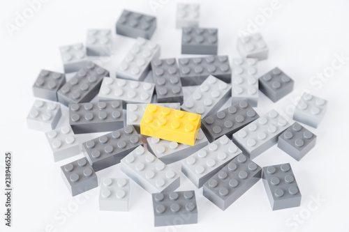 Pile of gray toy building bricks and one bright yellow brick on top of them on white background. Concept photo of standing out from the crowd or gray masses.