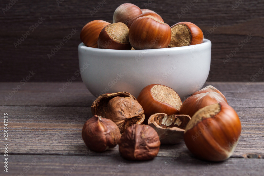 Obraz premium Filbert nuts in white porcelain bowl on wooden background