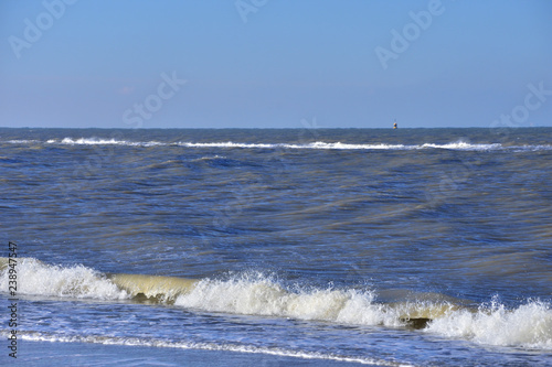 Morska fala z pianą atakuje piaszczystą plażę.