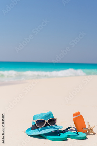 Suncream bottles, goggles, starfish and sunglasses on white sand beach background ocean