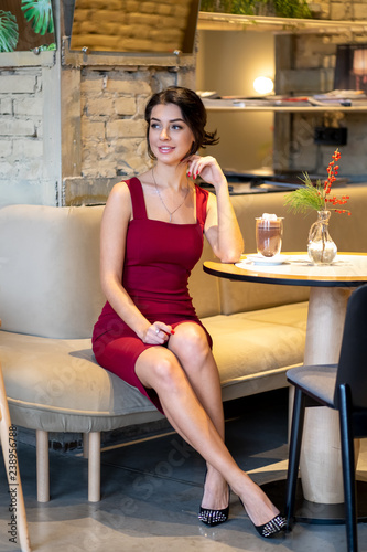 Young beautiful brunette girl sitting in a coffee with a cappuccino