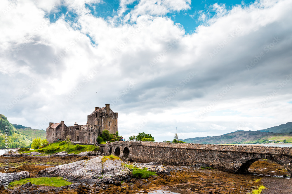 Eilean Donan Castle in the Highlands of Scotland on a cloudy day and low tide, ancient castle with sandstone bridge, lush nature with colorful moss and lichens 