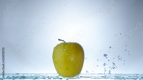 Green apple on a light background and splashing water