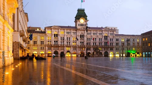Trieste, Italy. Unity of Italy Square in Trieste, Italy at night during the heavy raining. Illuminated buildings - town hall and cloudy sky. People with umbrellas. Day to night time-lapse, zoom in photo