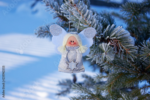 Christmas angel on a snowy branch of a Christmas tree. Handmade holiday decorations. Natural photo outdoors. Snowy weather. Winter vacation.