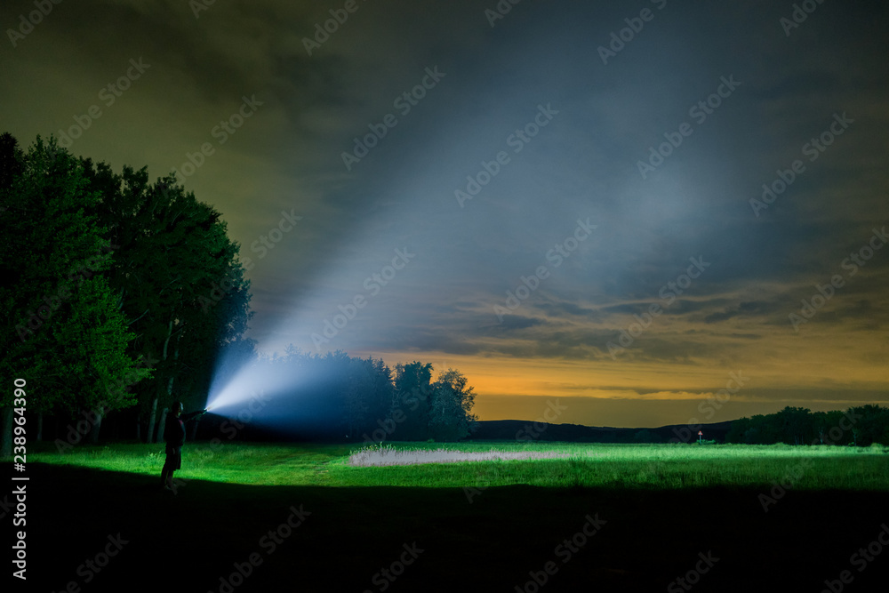 Man searching with flashlight on field by night	