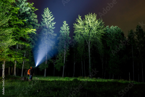 Man searching with flashlight in forest photo