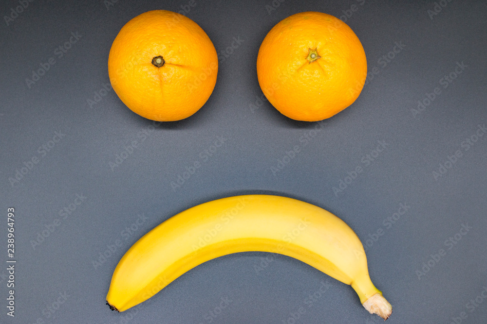 Unhappy, sad smiley face of fruits (oranges and banana), isolated on gray background