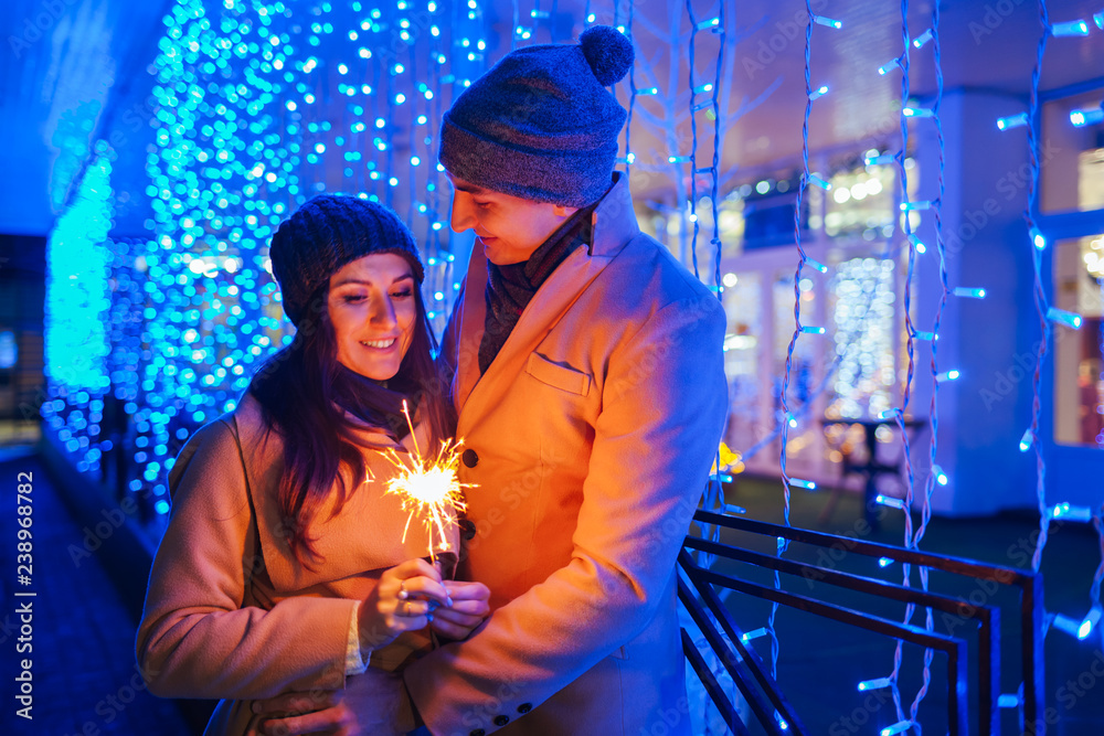 Fototapeta premium Young loving couple burning sparklers by holiday illumination