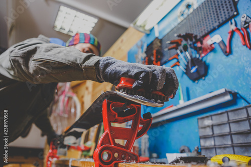 A man in work clothes, repairman in workshop ski service repairing the sliding surface of skis, Brushing, wax removal, final ski polishing. In the hands of an electric brush. Theme repair of ski curb photo