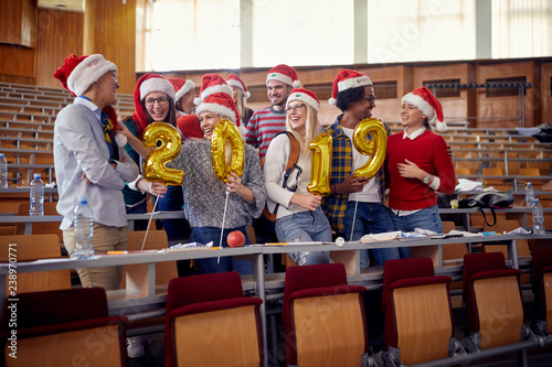 Students friends in Santa hat holding 2019 golden balloons at New Year party on university.