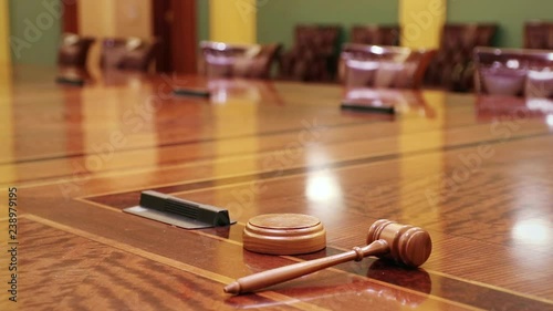 Wooden gavel resting on large table, with empty chairs in the distance.