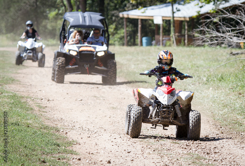 Child on quad ATV with parents in UTV on dirt road