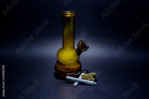 Obraz na płótnie An orange glass water bong full of smoke and a burning bowl with a small pile of Cheese OG marijuana buds next to it and 2 joints. w salonie
