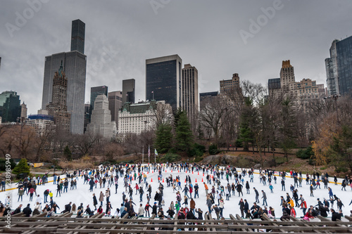 Many People enjoying themselves on a skating ring in Southern Central Park,  with the manhattan skyline in the Background.