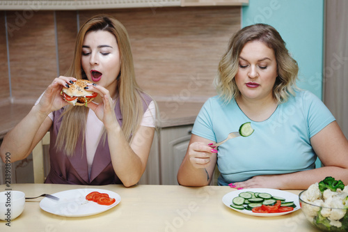 Two girlfriends of the woman in the kitchen are having fun and eating food.