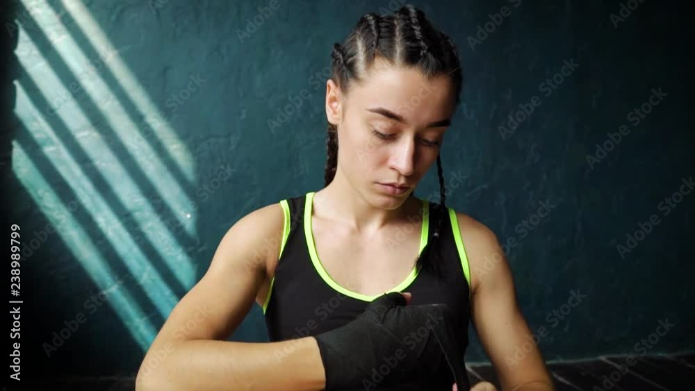 Slow motion panning fit young woman sitting on floor and wrapping hand with bandage. Female boxer athlete preparing for boxing training. wellness, fighting, motivation, self defense concept Slow motion panning fit young woman sitting on floor and wrapping hand with bandage. Female boxer athlete preparing for boxing training. wellness, fighting, motivation, self defense concept