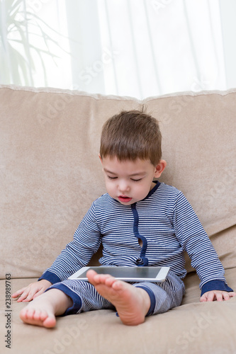 toddler boy is using a tablet on a couch