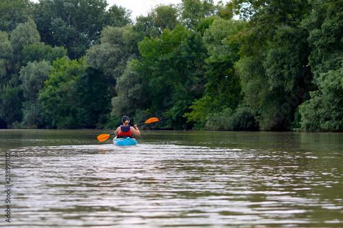 Kayaking. A Woman in blue kayak. Girl paddling in the calm summer Danube river near the shore with green trees