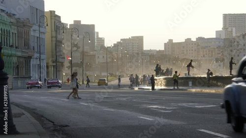 old 1950's Vintage classic american cars driving on famous waterfront malecon promenade, waves splash on fishermen, Old Havana, Cuba