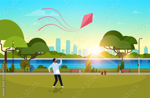young man launching kite outdoors modern public park guy playing wind toy holiday concept cityscape sunset background horizontal flat