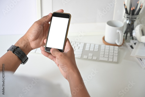 Mockup smartphone on man hands empty display with office desk background.