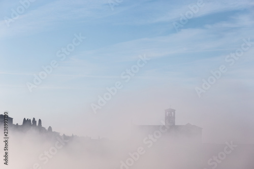 A view of a silhouette of St.Francis church in Assisi in the middle of mist beneath a blue sky with clouds