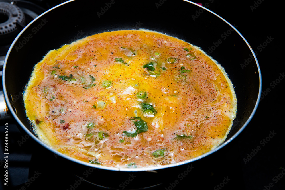 cooking omlette in Indian style with green chili , corriander leaves and lot of spices in a non stick pan cooking omlette in Indian style with green chili , corriander leaves and lot of spices in a non stick pan