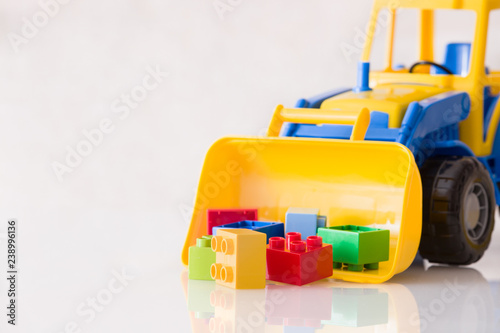 Colorful plastic bricks and children's toy tractor on a white background. Children's toys on the table are isolated.