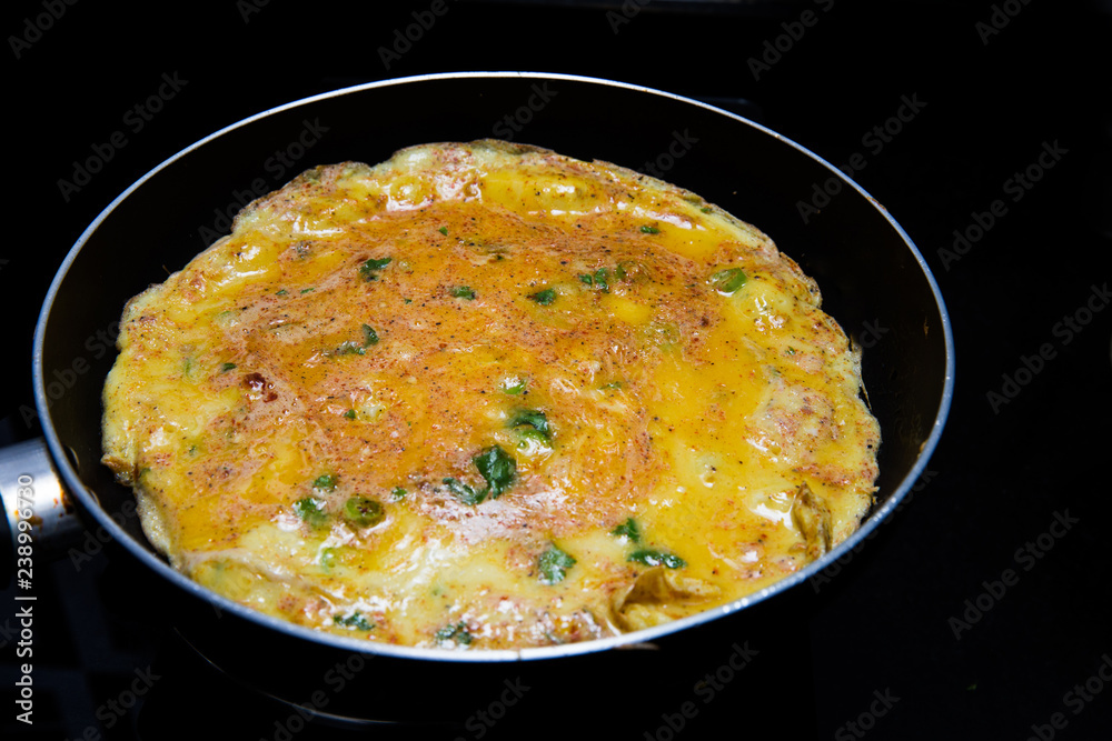 cooking omlette in Indian style with green chili , corriander leaves and lot of spices in a non stick pan cooking omlette in Indian style with green chili , corriander leaves and lot of spices in a non stick pan