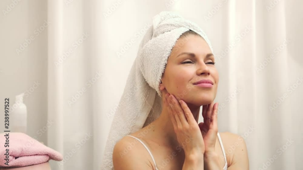 Beautiful female wrapped in towel after shower applying lotion. Skin care and cosmetics concept. Beautiful female wrapped in towel after shower applying lotion. Skin care and cosmetics concept.