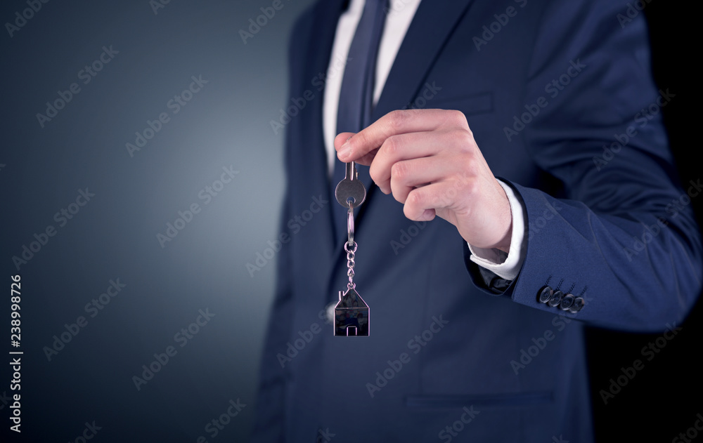 Young businessman hand over keys with empty dark background
Young businessman hand over keys with empty dark background