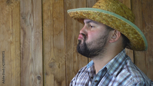 A grown man looks into the distance. Straw hat on his head. He's wearing a plaid shirt. Unshaven face. 