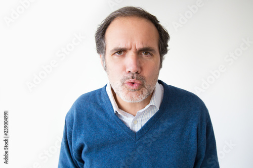 Mature Caucasian man pouting lips and looking at camera. Middle aged man in blue sweater blowing kiss. Isolated on white. Kissing concept © KAMPUS