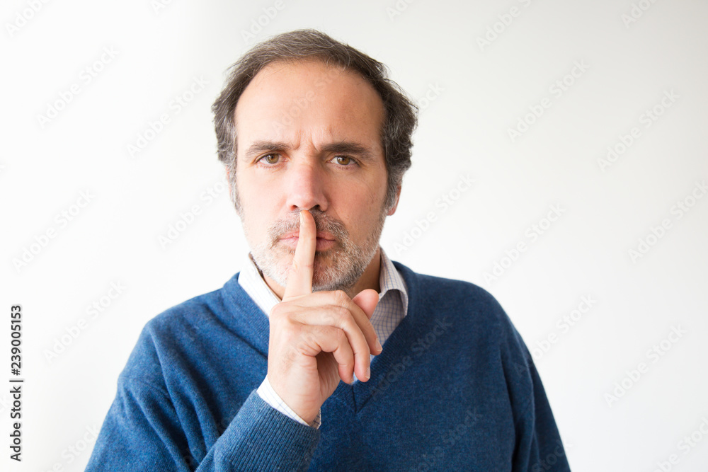 Serious Caucasian man with silence symbol, studio portrait. Confident man with grey hair in blue sweater. Isolated on white. Secret concept Serious Caucasian man with silence symbol, studio portrait. Confident man with grey hair in blue sweater. Isolated on white. Secret concept