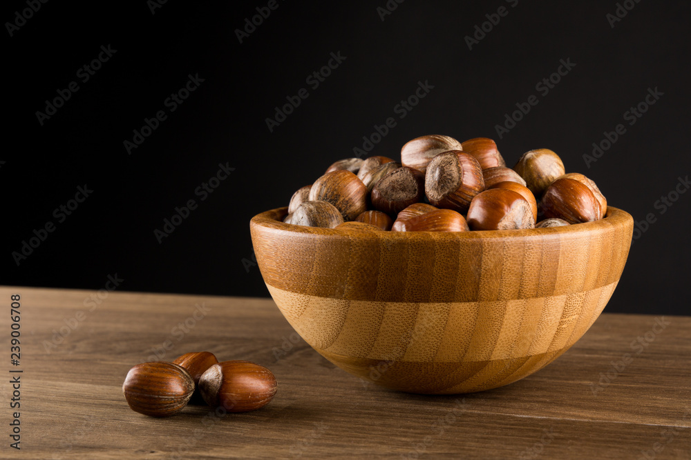 Obraz premium Hazelnuts in wooded bowl isolated on black background, copy space