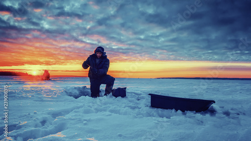 Fisherman on the background of the sunset on the winter lake. Ice fishing.