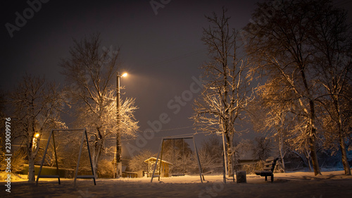 Beautiful rural winter snow-covered street with lanterns on. And light trails from cars