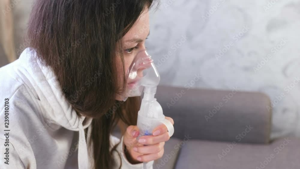 Use nebulizer and inhaler for the treatment. Young woman inhaling through inhaler mask. Close-up face, side view. Use nebulizer and inhaler for the treatment. Young woman inhaling through inhaler mask. Close-up face, side view.