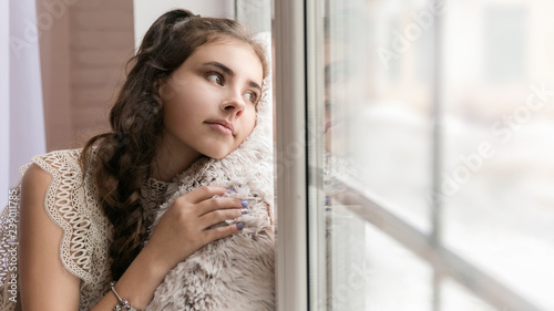 beautiful brunette girl sitting on the windowsill hugging a soft beige pillow and looking out the window Free Download beautiful brunette girl sitting on the windowsill hugging a soft beige pillow and looking out the window - GFXLoad