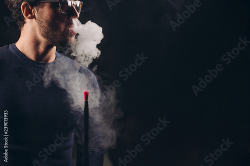attractive man exhaling smoke from the nose. close up side view shot.man in glasses advertising a hookah