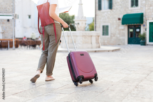 Girl traveler with pink suitcase and backpack at city street. Woman tourist is searching direction, sightseeing in old town. Concept of travel, vacation, female tourism, trip.