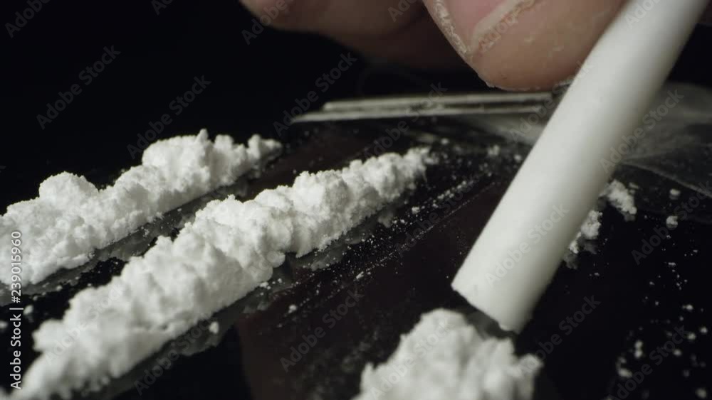 Lines of cocaine being snorted through tube on table top while moving over the white powered drug.