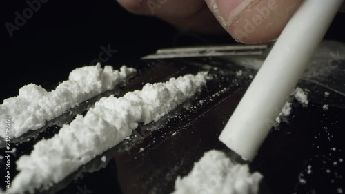 Lines of cocaine being snorted through tube on table top while moving over the white powered drug.