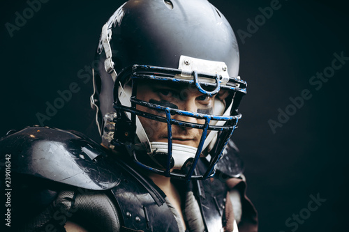 Shirtless American football player with wearing helmet and protective shields on naked body, half size portrait over black wall, close up