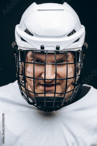 Portrait of hockey keeper in protective helmet with carbonic defence in white uniform grinning at camera over black background